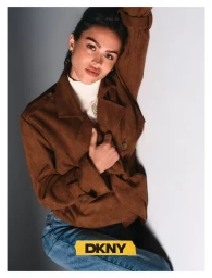 Model Amelia Gray in a brown belted coat leaning against a white studio wall for DKNY Fall 26 edit