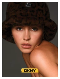 Model Iris Law wearing a brown animal print bucket hat and small hoop earrings against a dark grey background for DKNY