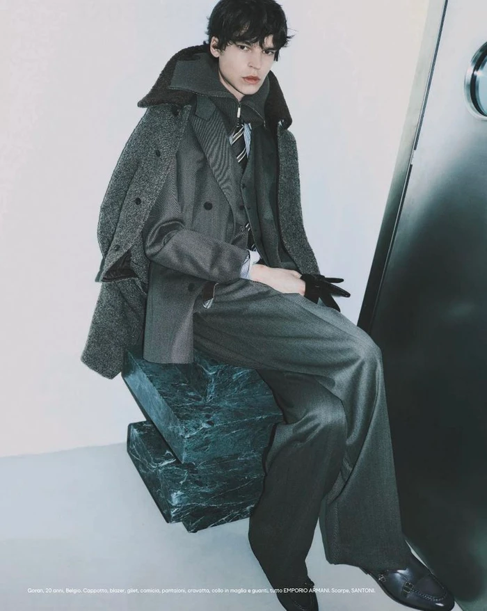 Model seated on a dark green marble block wearing a grey suit jacket and coat in an editorial for Esquire Italia.
