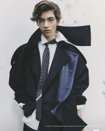 Young man wearing a dark coat, white shirt, and patterned tie against a plain white background for Esquire Italia.