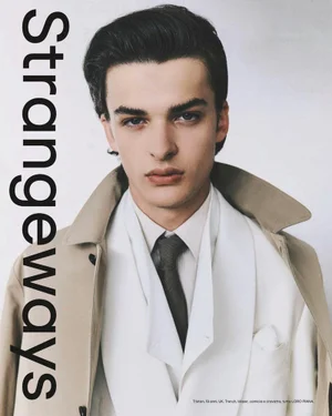 Portrait of a male model wearing a tan trench coat, white blazer, white shirt, and dark tie against a plain background