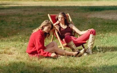 Two female models in red attire sitting on grass and in a deckchair outdoors for a Harper's Bazaar U.S. fashion editorial.