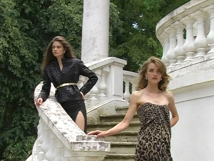 Two female models posing on a white stone staircase with classical balustrades outdoors