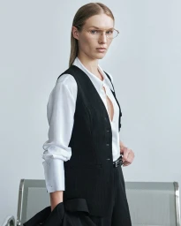 Model wearing a white shirt and black vest with eyeglasses against a light grey studio background.