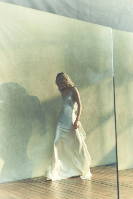 Model Aivita Mūze in a white satin slip dress standing against a pale textured wall for Danielle Frankel S/S 27.