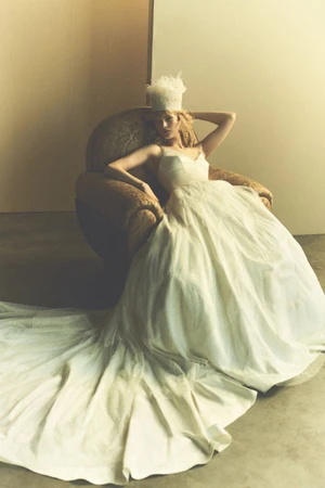 Model seated in an armchair wearing a white bridal gown and feathery headpiece for Danielle Frankel S/S 27.