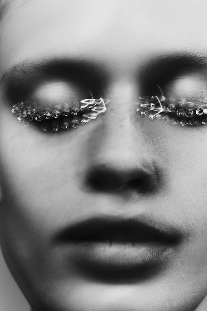 Close-up portrait of a model with dramatic eye makeup and beaded eyelashes in black and white for H and M