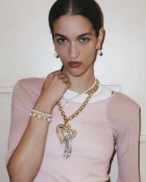 Model wearing layered gold necklaces and pearl earrings against a neutral background for Mimco July