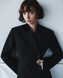Model Lily Vander Meeden wearing a black tailored blazer adorned with a gold heart brooch against a pale studio backdrop.