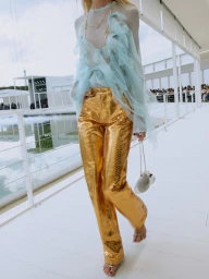 Model in metallic gold trousers and sheer ruffled pale blue top walking along a white runway pavilion.