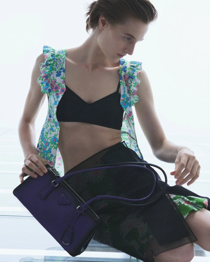 Model Lana Petkovski holding a purple handbag, wearing a floral strap top and black skirt for Prada.