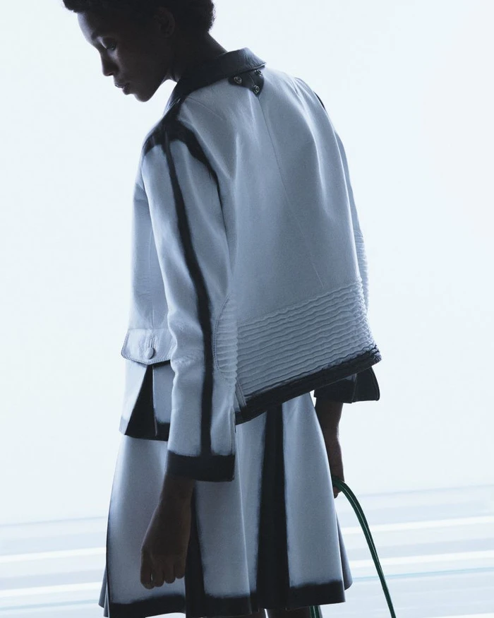 Model wearing a white structured jacket and matching skirt with dark trim against a pale background