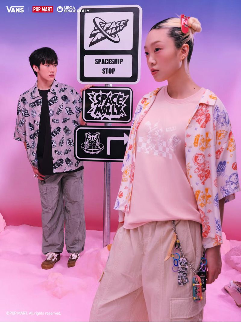Two Asian models showcase a Vans x Pop Mart fashion collaboration against a pink and blue set with streetwear and signage.