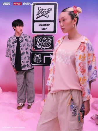 Two Asian models showcase a Vans x Pop Mart fashion collaboration against a pink and blue set with streetwear and signage.