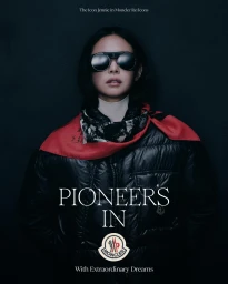Jennie wearing dark sunglasses, a white turtleneck, a red scarf, and a black puffer jacket against a dark background.