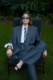 Frankie Rayder seated outdoors in an oversized charcoal grey suit, tie, and sunglasses for Saint Laurent Fall 2025.