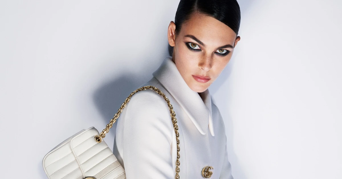 Vittoria Ceretti wearing white coat with gold chain handbag against white background
