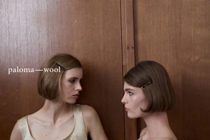 Two women with short bob hairstyles and hair clips posing against a wooden paneled wall for Paloma Wool