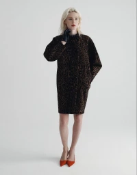 Model with blonde hair wearing an animal-print coat and red heels standing against a seamless white background.