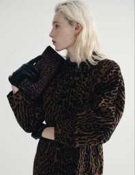Model with blonde hair wearing a leopard print dress and black leather gloves holding a matching clutch bag