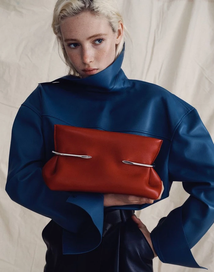 Model Summer Dirx in a blue high-neck top holding a red leather clutch for Saks