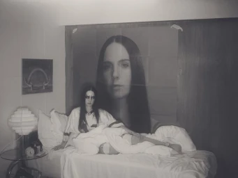 Woman in sports jersey and dark makeup seated on a white bed with a large poster behind her by Casper Sejersen