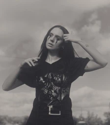 Singer MØ with running black eye makeup wearing a sequin corset and black t-shirt outdoors against an overcast sky.