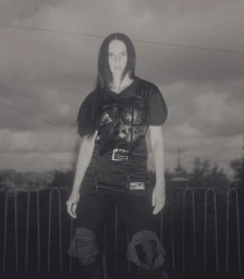 Woman in dark athletic apparel and lace corset top posing outdoors against an overcast sky and metal fence.