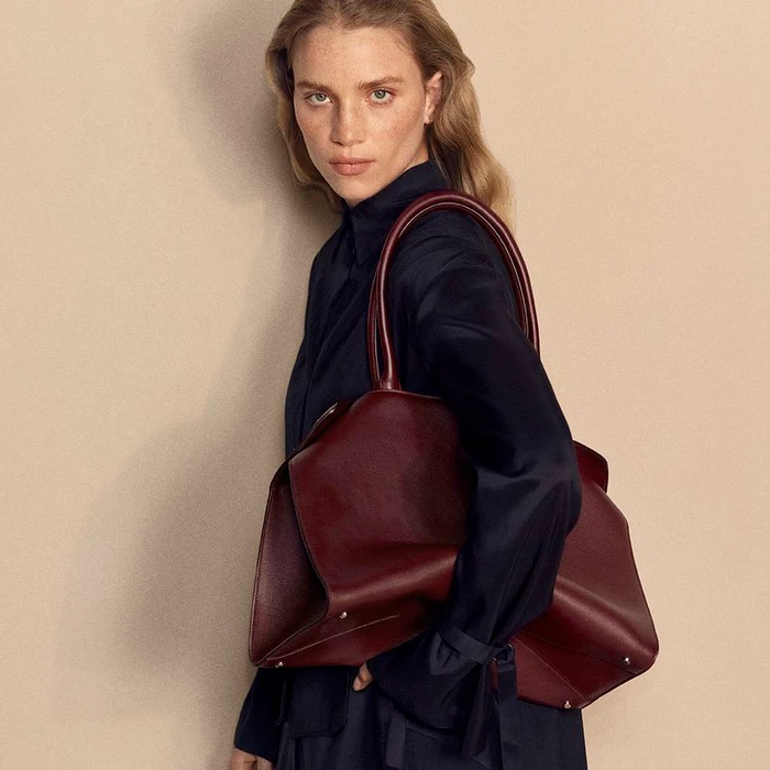 Model Rebecca Leigh Longendyke holding a burgundy leather tote bag in a portrait for Cartier shot by Mark Kean.