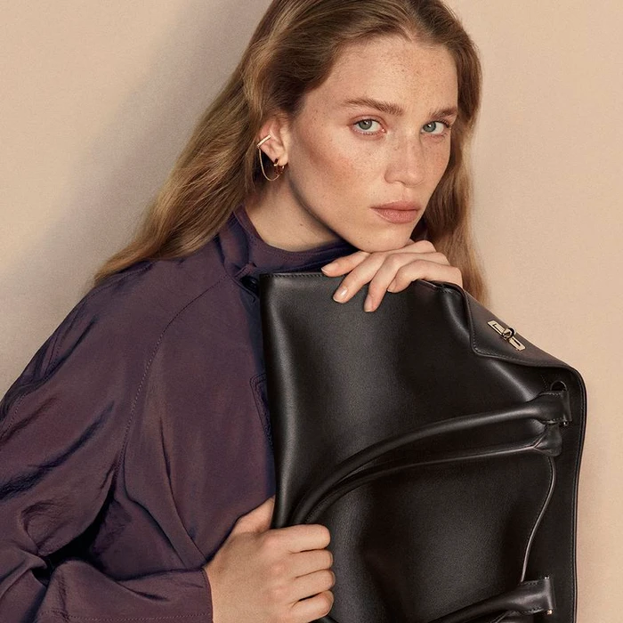 Model Rebecca Leigh Longendyke in purple top holding black leather tote bag for Cartier