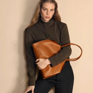 Model Rebecca Leigh Longendyke holding a tan leather Cartier tote bag against a neutral background