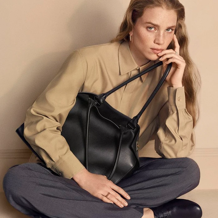 Model Rebecca Leigh Longendyke in a beige shirt holding a black leather tote bag for Cartier by photographer Mark Kean.