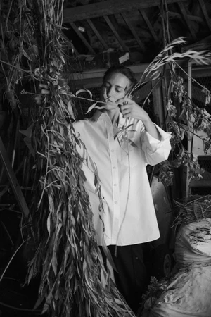 Model in white shirt holding hanging dried foliage inside a rustic wooden barn
