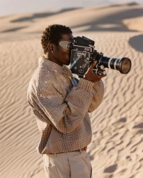 Black man holding a vintage movie camera filming in a sandy desert landscape