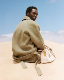 Model Monykuoch Deng in an olive wool coat with a cream handbag on sandy dunes under a clear blue sky