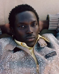 Portrait of a black male model wearing a houndstooth jacket with sequin embellishments and a yellow collared shirt