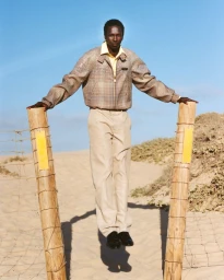 Model Monykuoch Deng jumping between wooden fence posts in a sandy dune landscape for At Large Magazine.