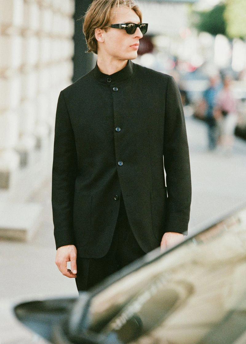 Young man wearing black jacket and sunglasses standing outdoors near a vehicle for Le Figaro editorial.
