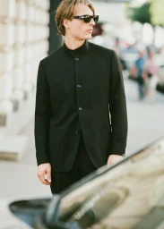 Young man wearing black jacket and sunglasses standing outdoors near a vehicle for Le Figaro editorial.