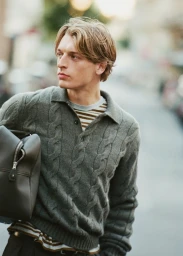 Model Colin Otto wearing a cable knit polo sweater and carrying a dark bag outdoors for Le Figaro, photographed by Valentin Hennequin.