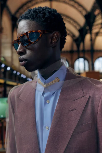 Black man wearing tortoiseshell sunglasses, light blue button shirt with embroidery, and mauve blazer for Valentino SS27 BOH