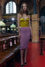 Model standing in a library wearing a yellow bustier and pink midi skirt for Valentino SS27 backstage by Fran Gomez de Villaboa