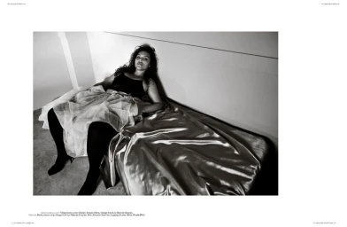 Model reclining on a shiny satin bed wearing a dark top and layered skirt with tights