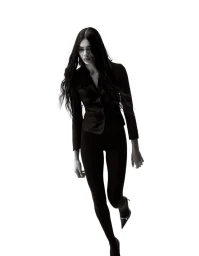 Model with long dark wavy hair wearing a black jacket and leggings against a white background