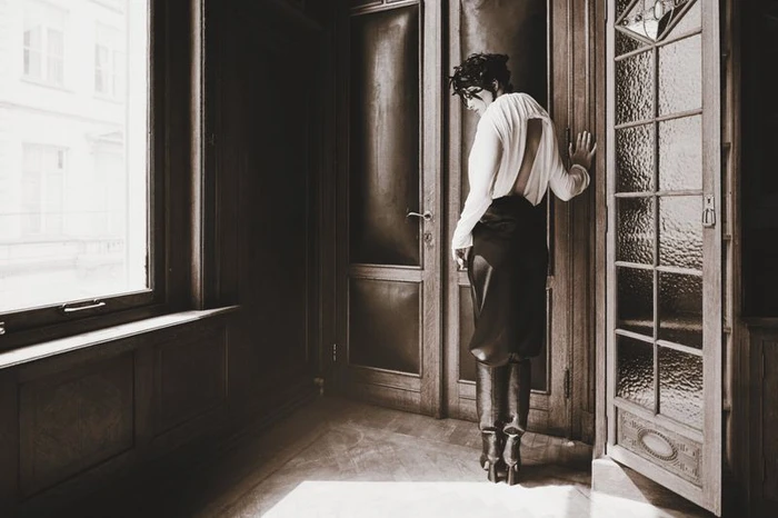 Woman in white blouse and dark skirt standing by a wooden doorway in an interior space
