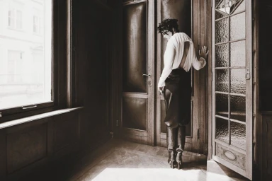 Woman in white blouse and dark skirt standing by a wooden doorway in an interior space
