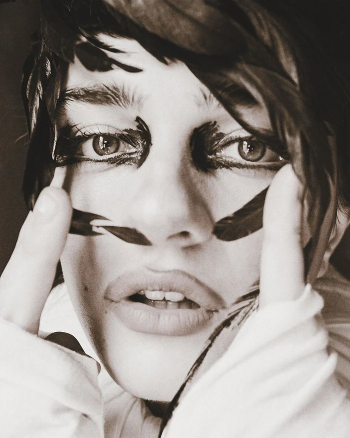 Close-up portrait of a model with dark feathers framing her face and bold black eye makeup for SHADOWPLAY Magazine