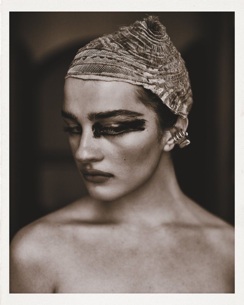 Portrait of a model wearing a textured patterned head covering and dark eye makeup with silver ear cuffs for SHADOWPLAY Magazine.