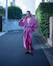 Model Song Ah Woo in an oversized pink hooded coat walking down a narrow residential street for Exhibition Magazine