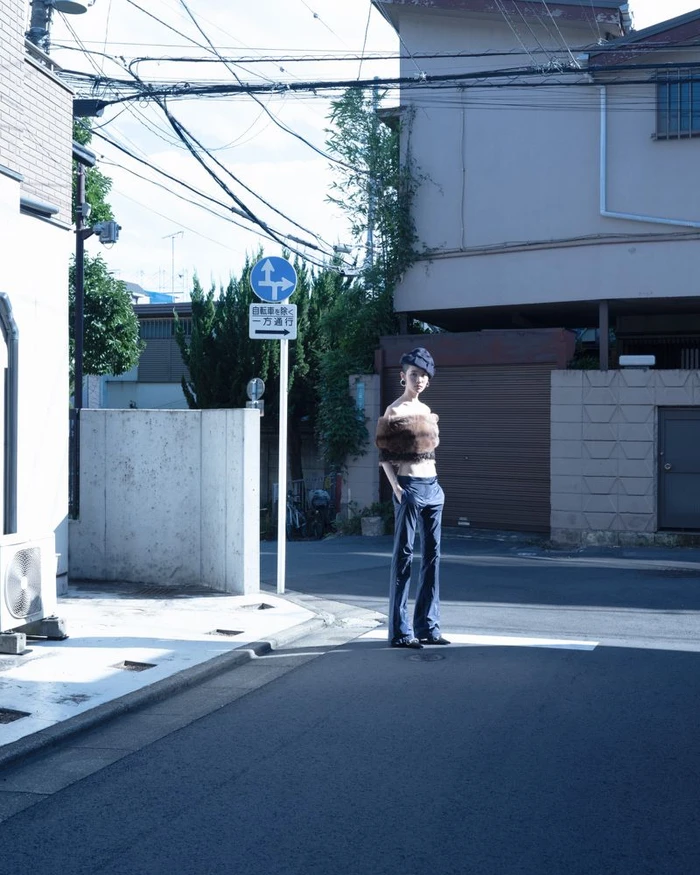 Model standing on a city street wearing an off-shoulder fur top and trousers near a road sign.